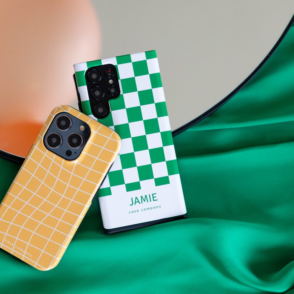 İki sağlam kılıf: iPhone için sarı ekose desenli bir kılıf ve üzerinde Jamie adı yazan yeşil kare desenli bir kılıf